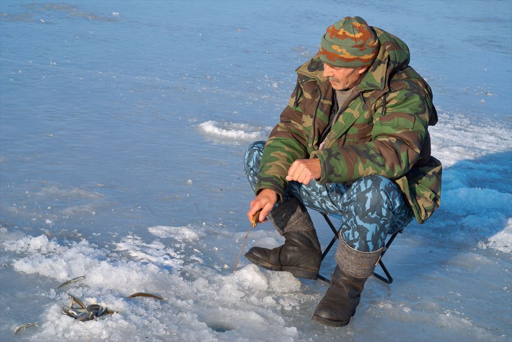 A man on winter fishing on ice of river. Season of smelt fishing.